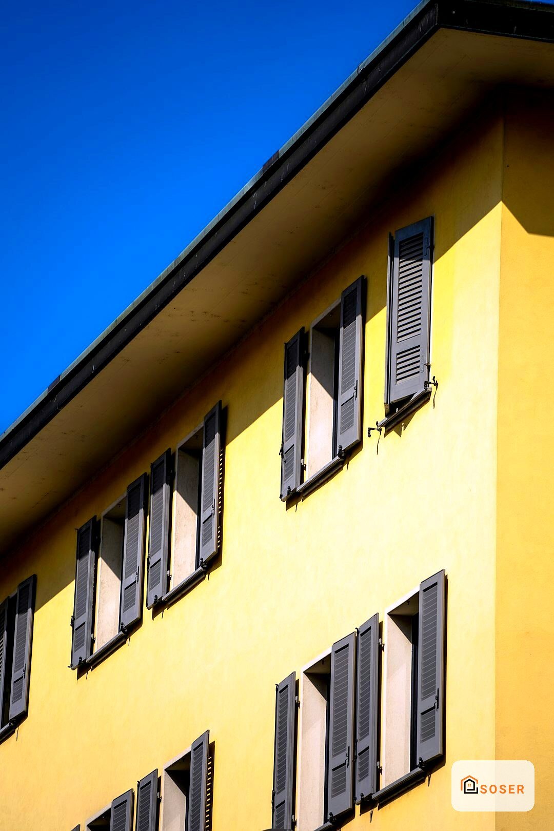 Facciata di edificio giallo con finestre e shutters grigio scuro su cielo blu