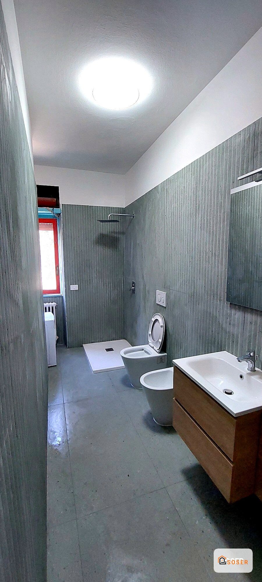 Bagno moderno ristrutturato con piastrelle grigie, lavabo in legno e illuminazione LED a Milano