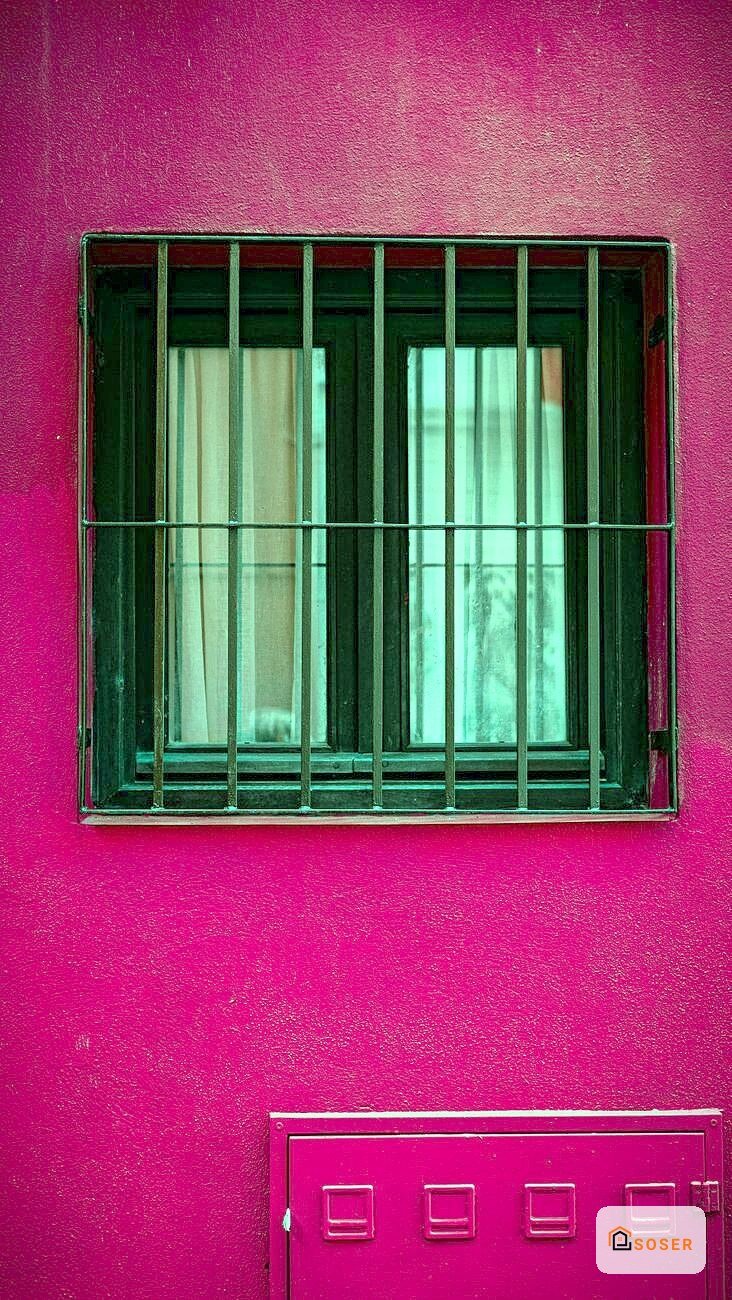 Facciata di edificio con parete fucsia e finestra con infissi verdi e persiane