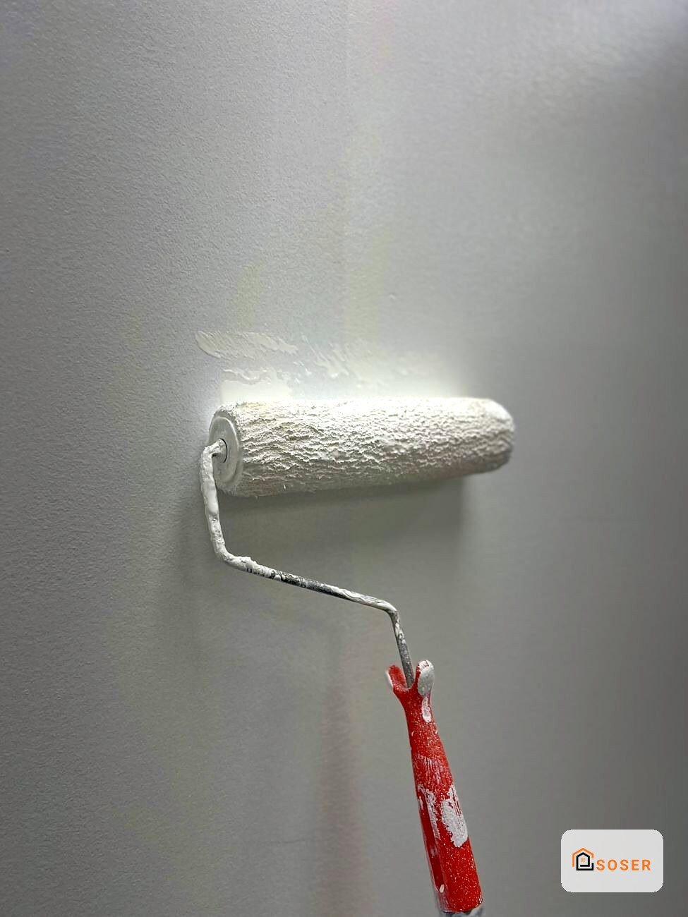 Rullo per pittura bianca su parete grigia durante lavori di imbiancatura