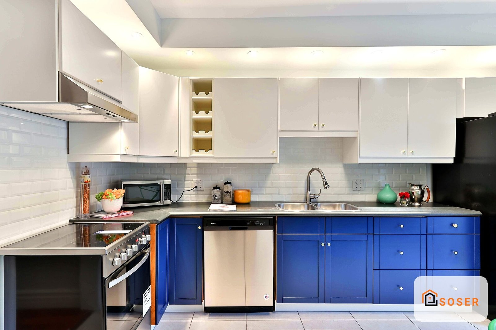 Cucina moderna con mobili blu e bianchi, piano in acciaio inox e piastrelle grigie