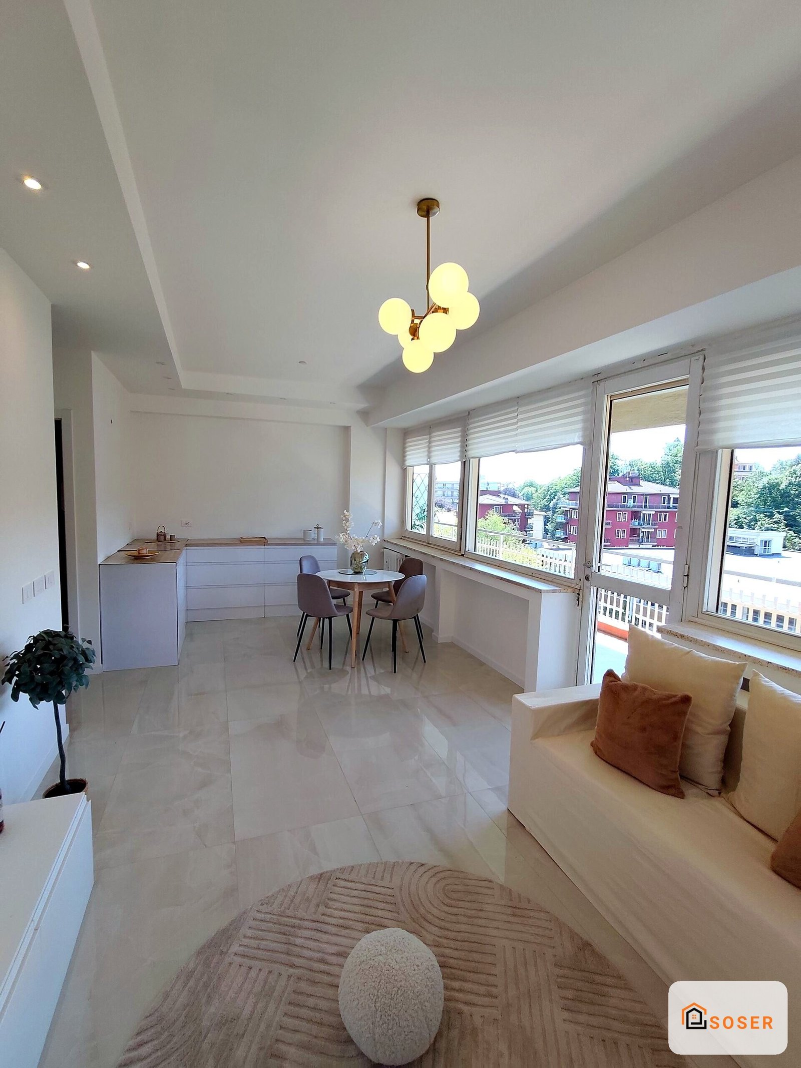 Appartamento moderno con cucina bianca, tavolo da pranzo e divano beige con vista sulla città