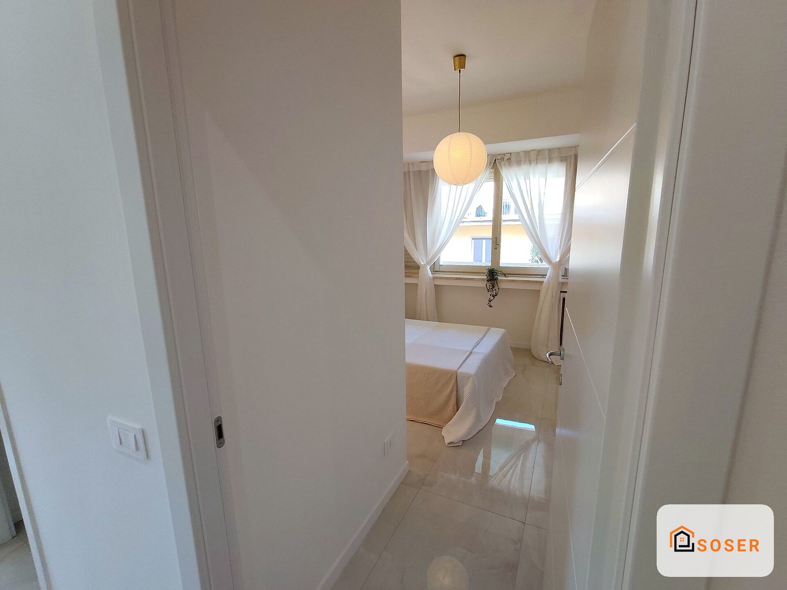 Corridoio moderno con pavimenti in marmo, pareti bianche e porta in cartongesso, illuminato da lampada a sospensione
