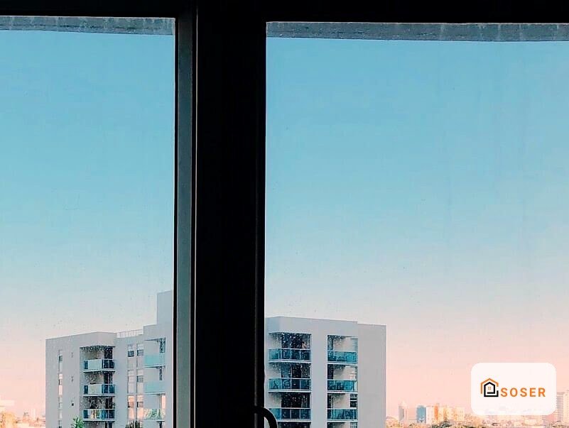 Vista dall'interno di un moderno appartamento con ampio infisso a vetrata che affaccia su edifici residenziali milanesi al tramonto
