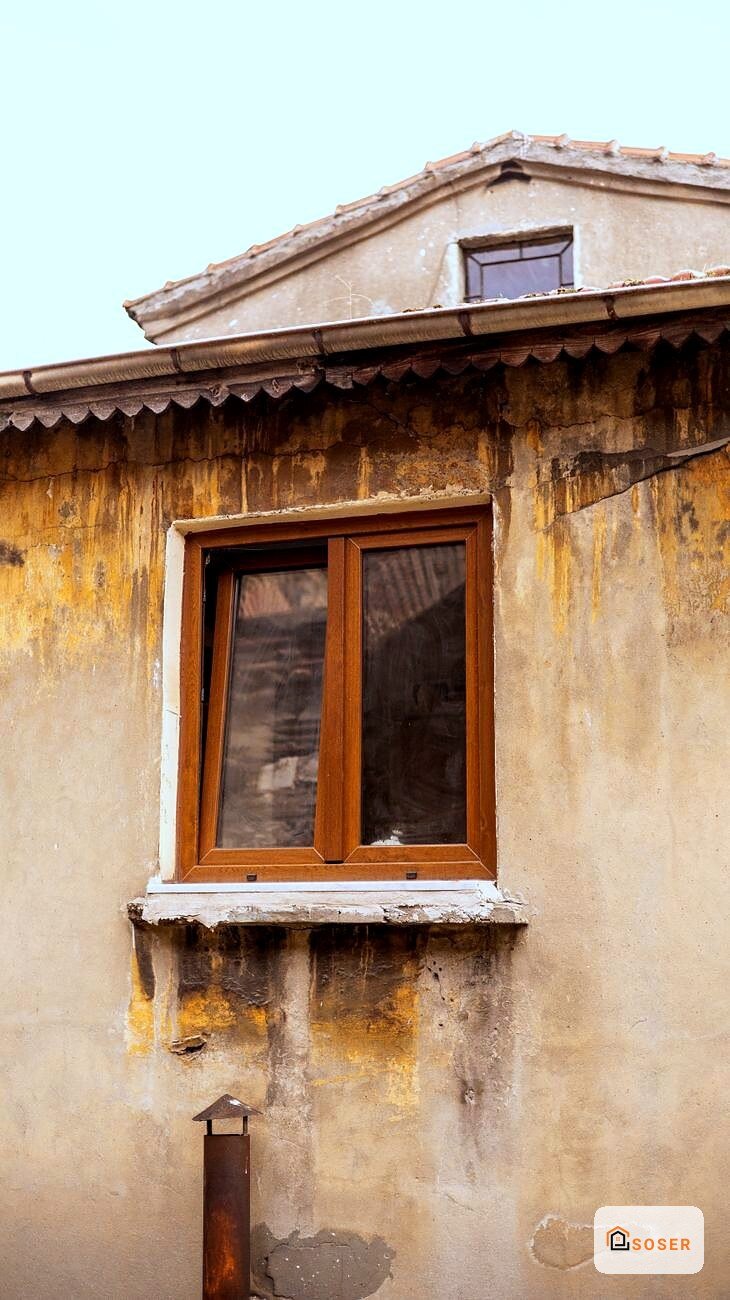 Facciata di edificio antico con intonaco deteriorato e finestra in legno