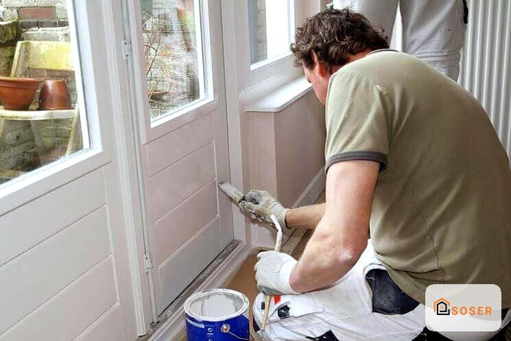 Operaio che vernicia la porta d'ingresso bianca con pennello durante i lavori di ristrutturazione