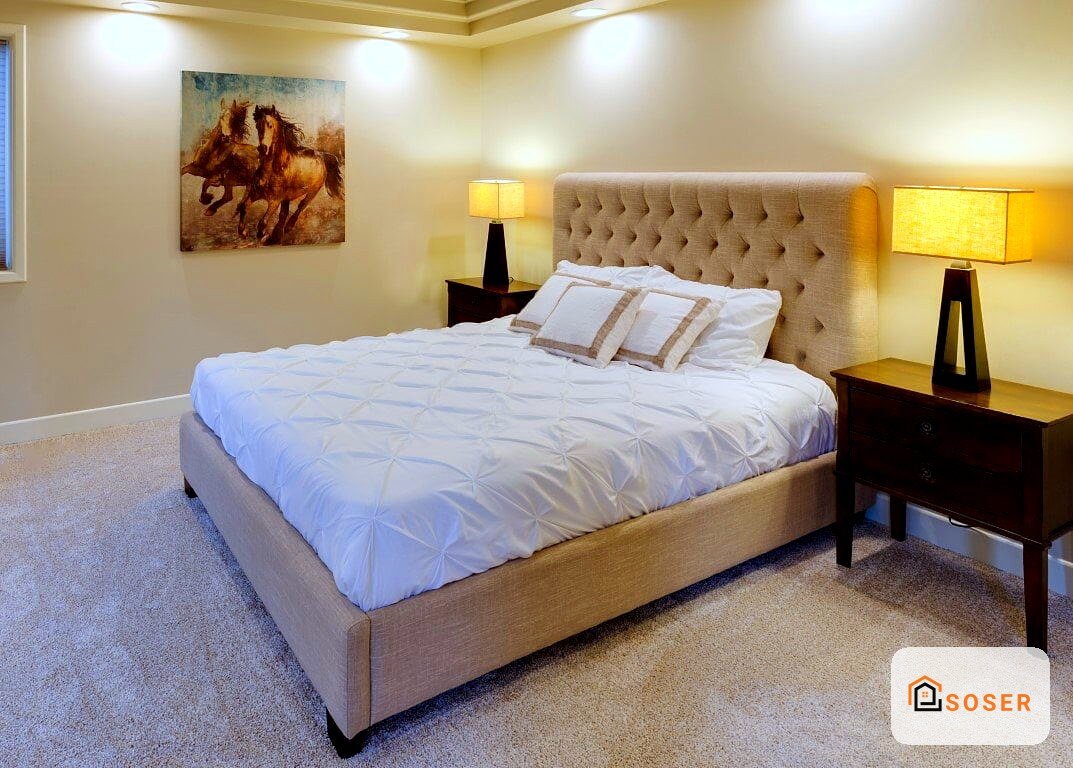 Camera da letto moderna con testata imbottita beige, letto bianco e lampade nere, pareti chiare