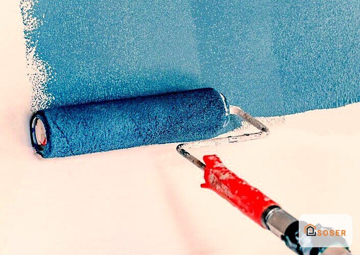 Rullo di pittura blu e pennello rosso durante lavori di imbiancatura su parete
