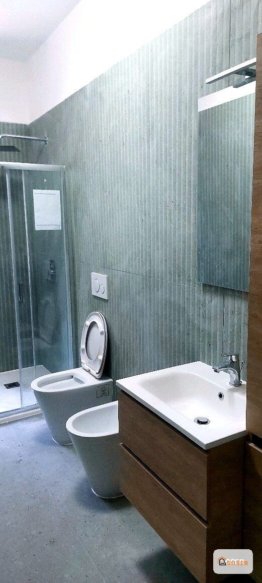 Bagno moderno con lavabo bianco, toilette e piastrelle verde acqua dopo ristrutturazione