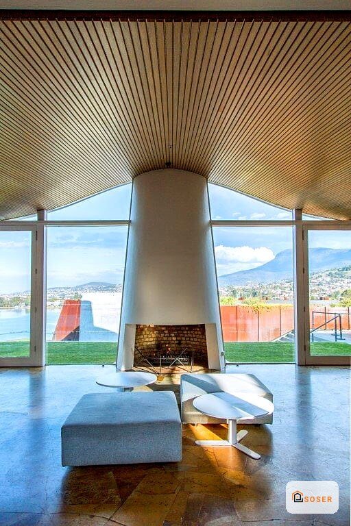 Soggiorno moderno con soffitto in legno, camino centrale e ampie vetrate panoramiche su paesaggio montano