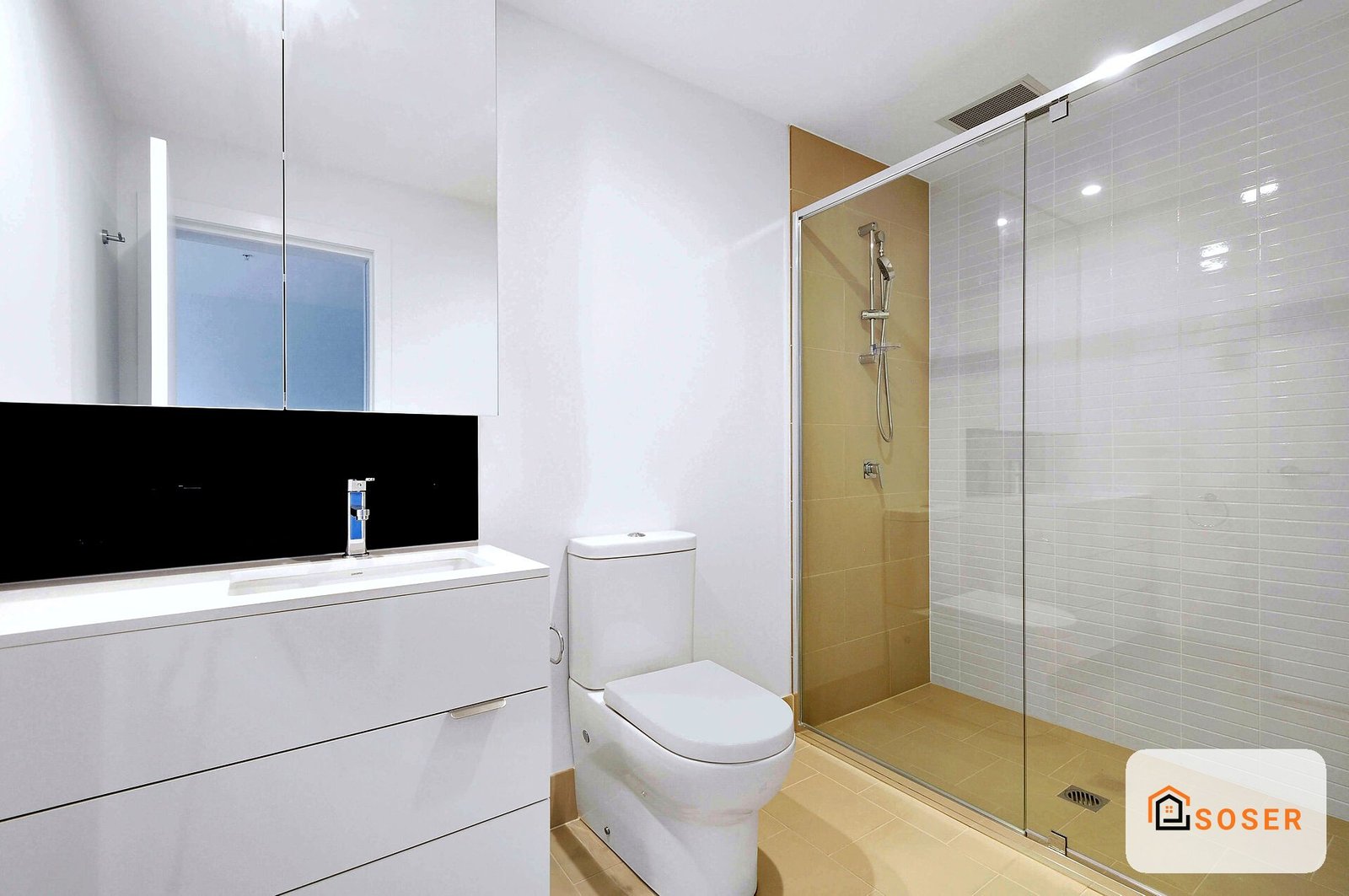 Bagno moderno con doccia in vetro, rivestimento in tonalità dorate e bianche, specchio illuminato sopra lavabo