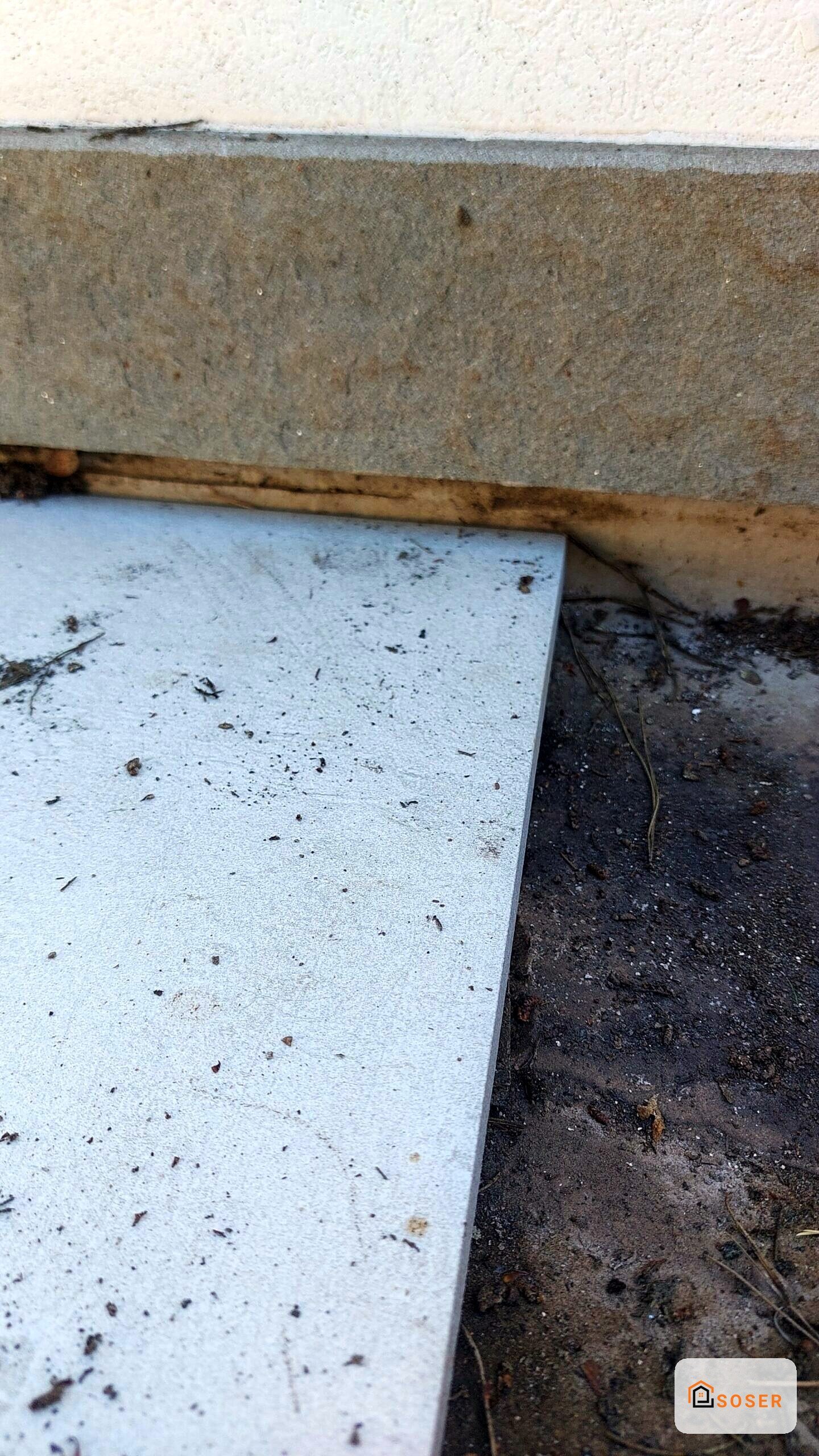 Dettaglio di pavimento in cemento grigio con battiscopa in legno e parete intonacata