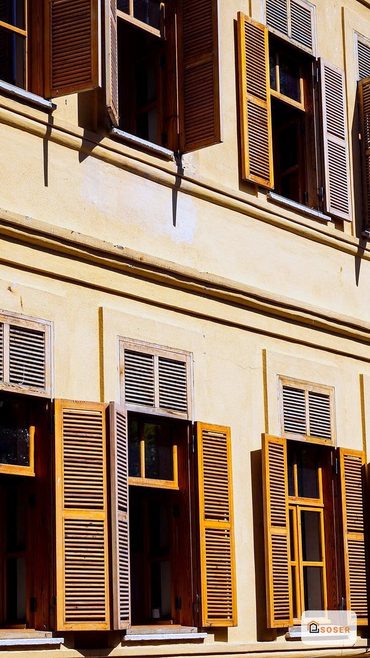 Facciata di edificio storico con persiane in legno giallo e marrone su muro color sabbia