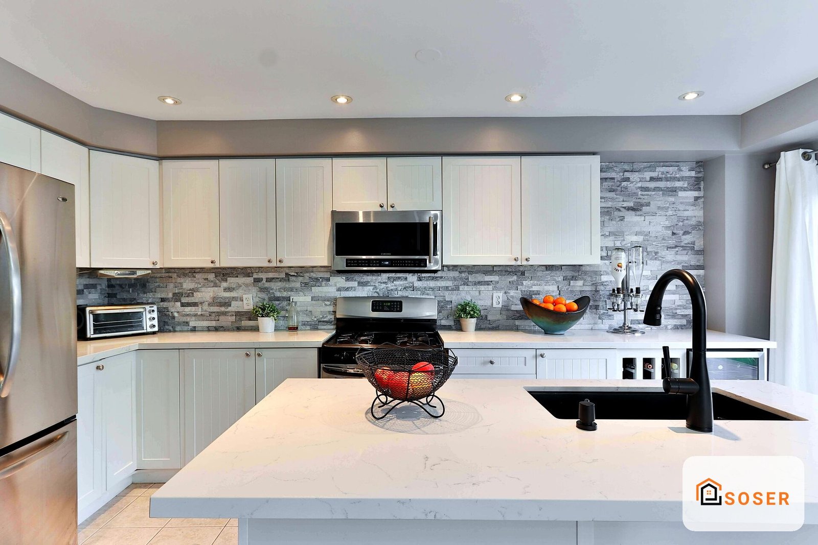 Cucina moderna con isola centrale, armadi bianchi, top in marmo bianco e backsplash in pietra grigia