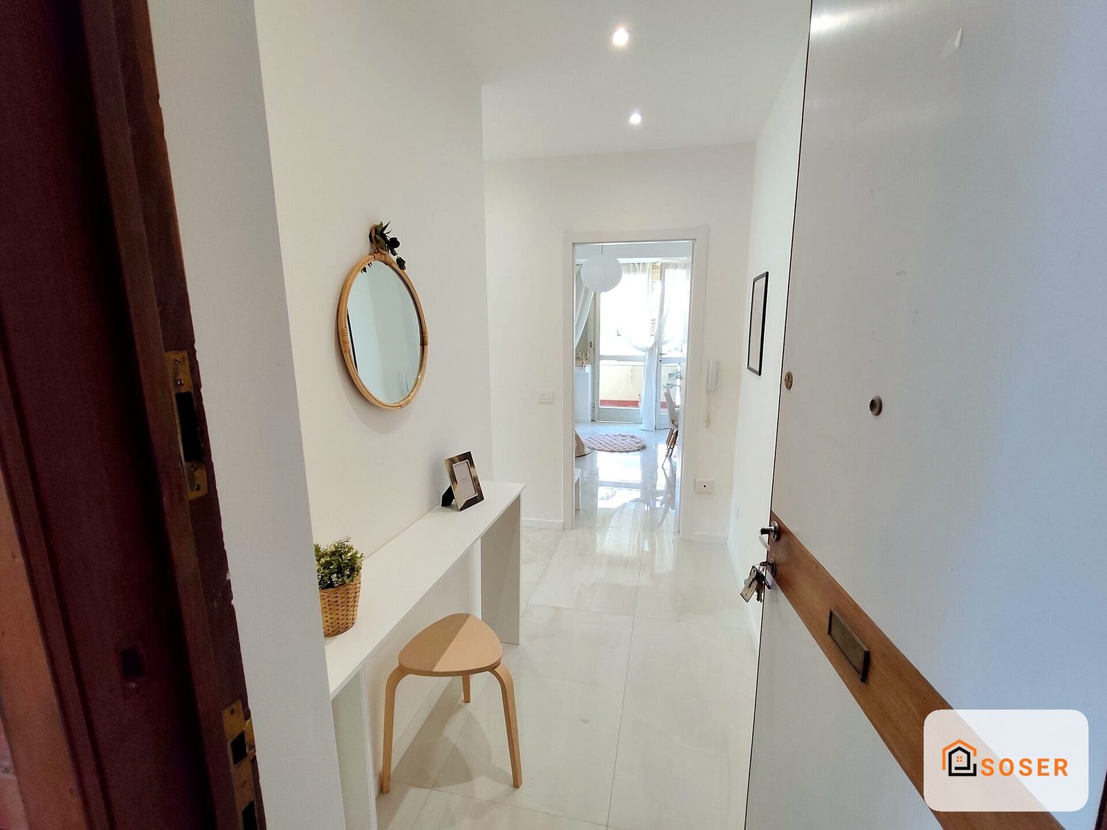 Ingresso moderno e luminoso con pavimento bianco lucido, specchio rotondo e consolle in stile minimalista