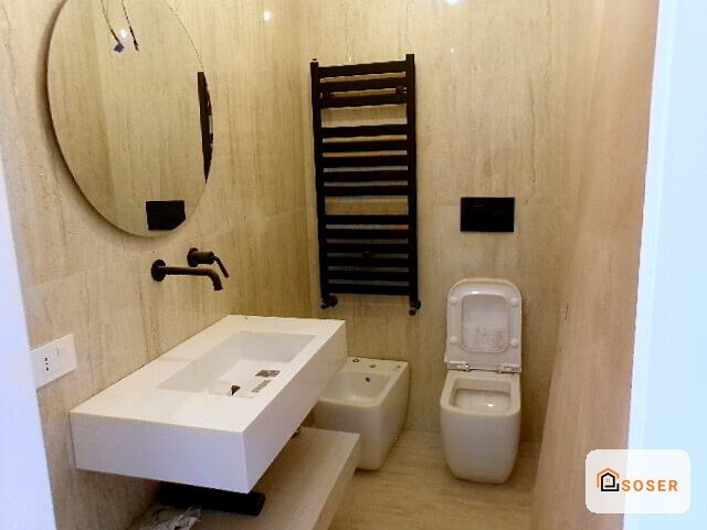 Bagno moderno ristrutturato con lavabo sospeso, specchio, radiatore scaldasalviette e pavimenti in ceramica beige