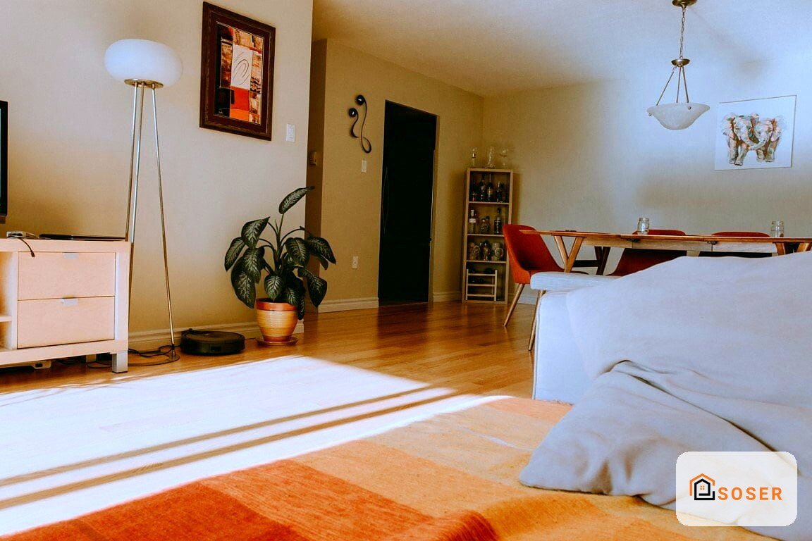 Ampio open space moderno con pavimenti in legno, letto con testata arancione e zona living con tavolo in legno e sedie rosse