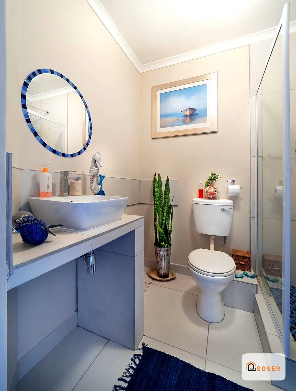 Bagno moderno ristrutturato con vanità blu, specchio circolare decorativo e pianta verde