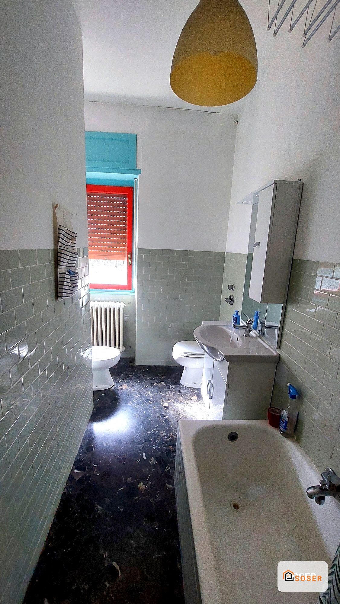 Bagno prima della ristrutturazione con piastrelle grigie e pavimento scuro