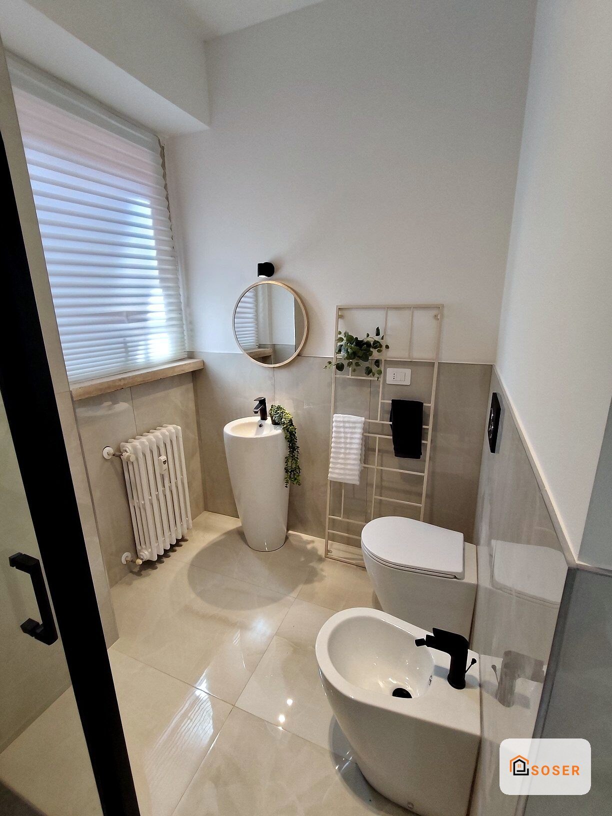 Bagno moderno con lavabo colonna, specchio rotondo e radiatore bianco, pavimento in gres porcellanato lucido
