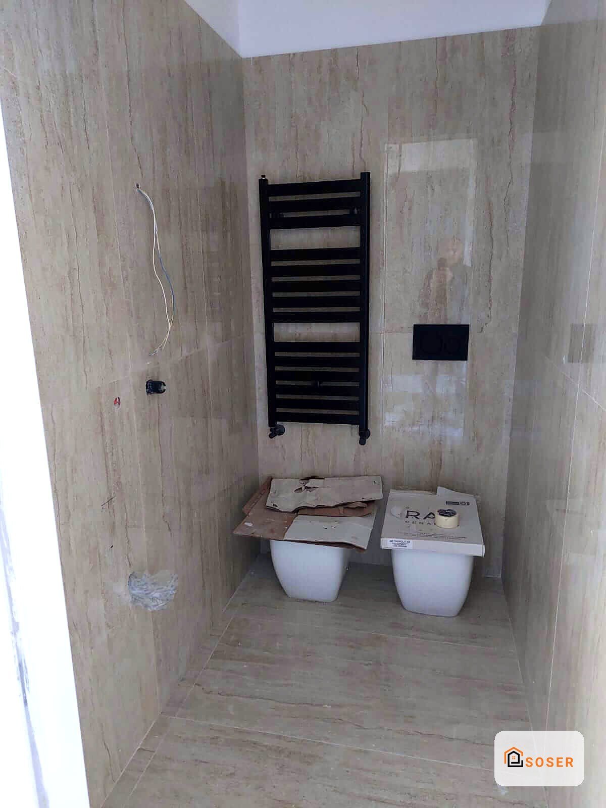 Bagno in ristrutturazione con piastrelle in corso d'opera, scaldasalviette nero e sanitari provvisori