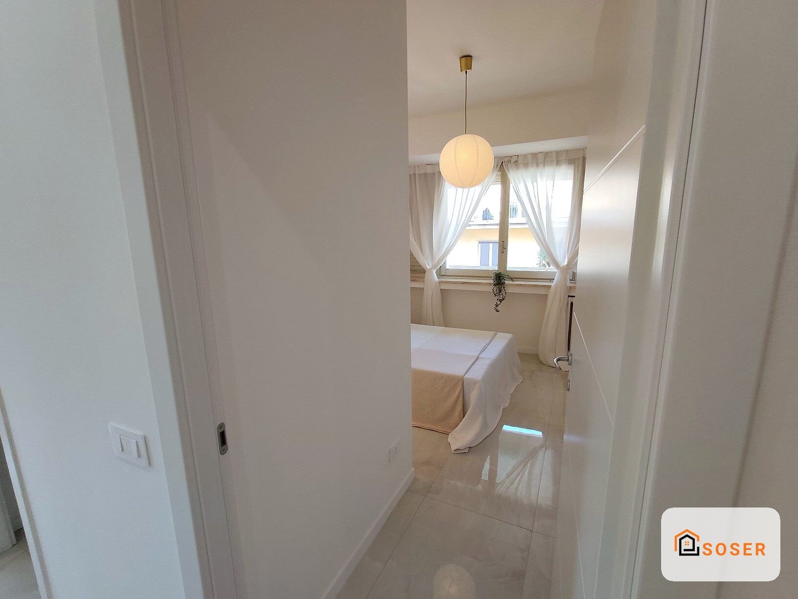 Corridoio luminoso con pavimenti in gres porcellanato beige e pareti imbiancate, con pendente moderno