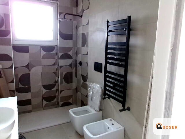 Bagno moderno ristrutturato con piastrelle geometriche, sanitari bianchi e scaldasalviette nero
