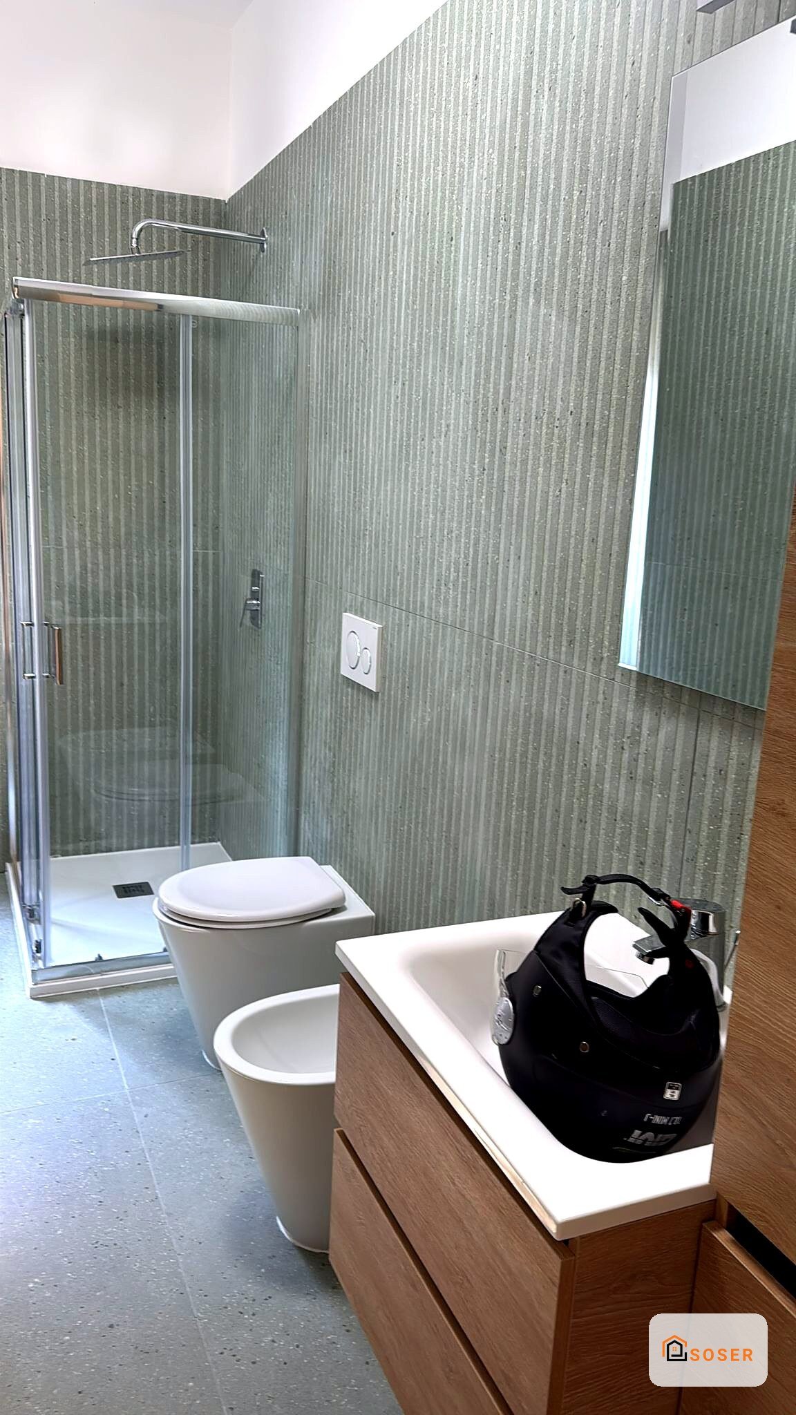 Bagno moderno con rivestimento in gres verde, lavabo in legno, toilet sospeso e doccia con box in vetro