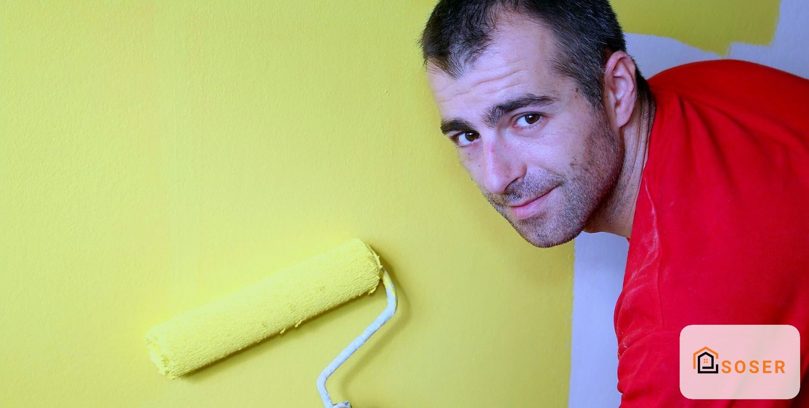 Operaio con rullo giallo che dipinge parete durante imbiancatura