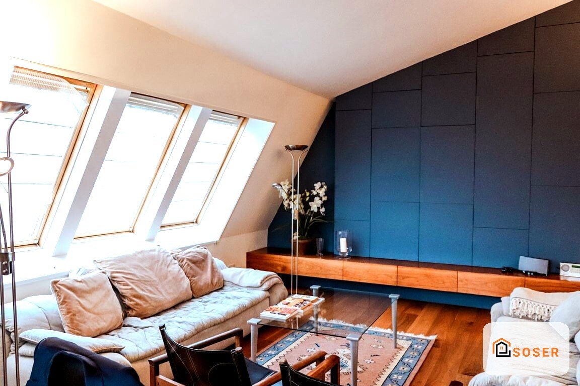 Mansarda ristrutturata con parete blu, pavimento in legno, finestre mansardate e arredamento moderno